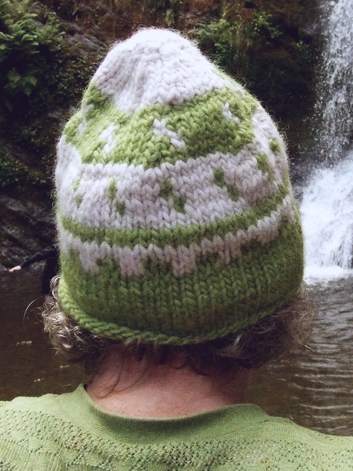 Person wearing green and white knitted hat near waterfall.