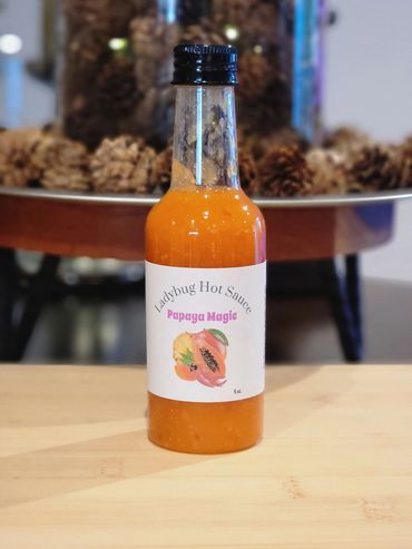 A bottle of Ladybug Hot Sauce Papaya Magic on a wooden surface.