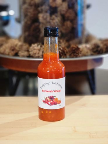 A bottle of Ladybug Hot Sauce Screamin' Ghost on a wooden surface.