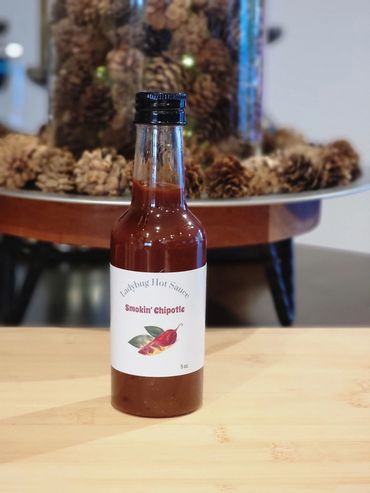 A bottle of Ladybug Hot Sauce Smokin' Chipotle on a wooden table.