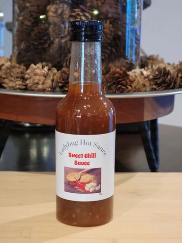 Bottle of Ladybug Hot Sauce Sweet Chili Sauce on a wooden table.