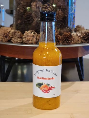 Bottle of Ladybug Hot Sauce Thai Mandarin on a wooden surface.