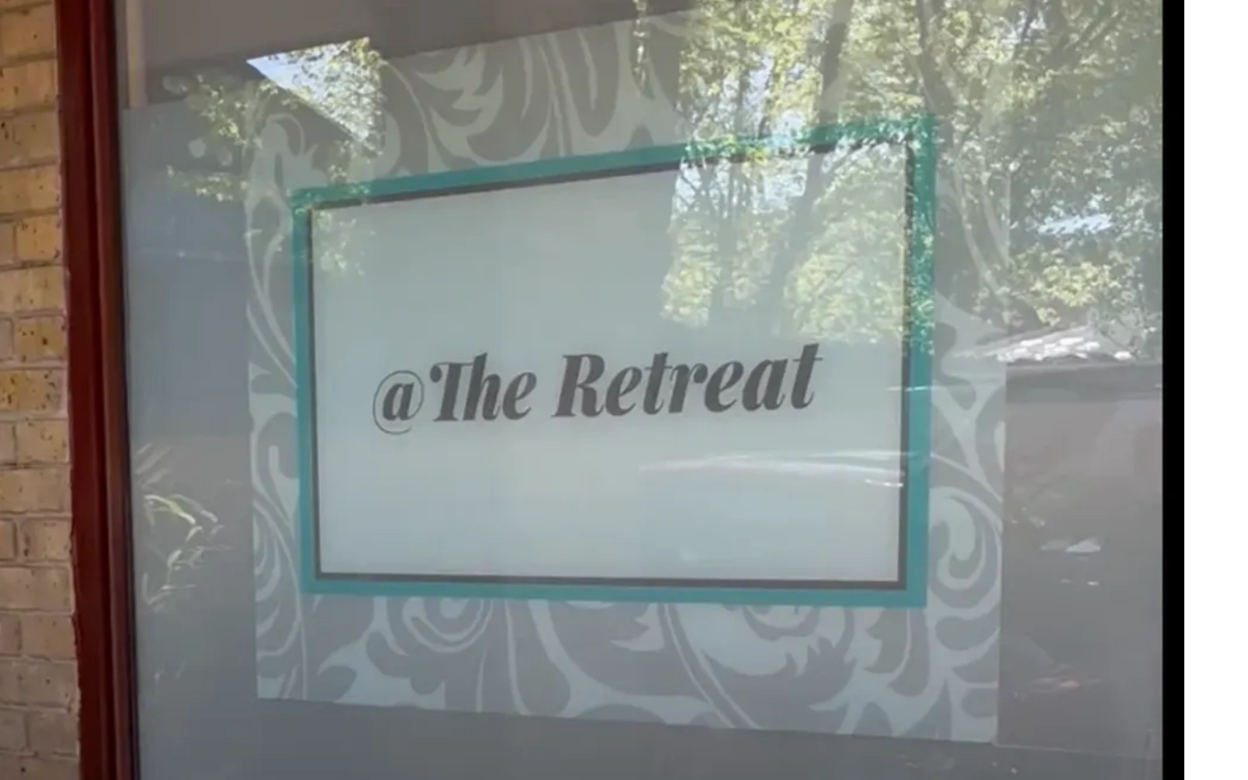 Window sign displaying '@The Retreat' with decorative background.
