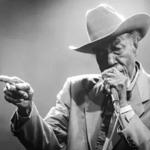 Elderly man playing harmonica and pointing.