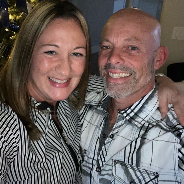 Smiling couple wearing patterned shirts, posing closely together indoors.