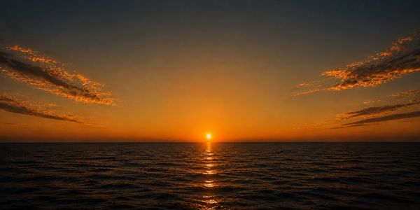 Sunset over calm ocean with vivid orange sky and scattered clouds.