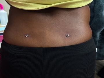 Two heart-shaped dermal piercings on the lower back.