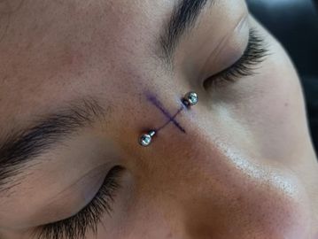 Close-up of a nose piercing with a cross mark.