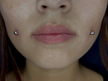 Close-up of lips and cheek piercings.