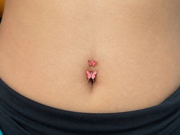 Belly button piercing with two pink butterfly charms.
