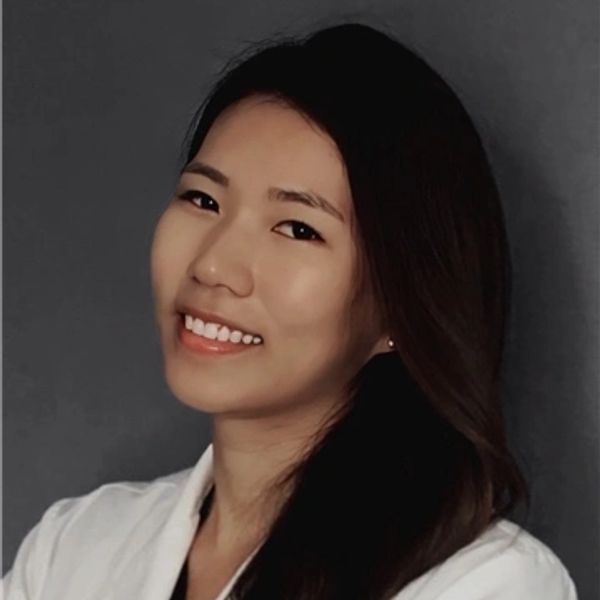 Smiling woman with long dark hair wearing a white shirt against a gray background.