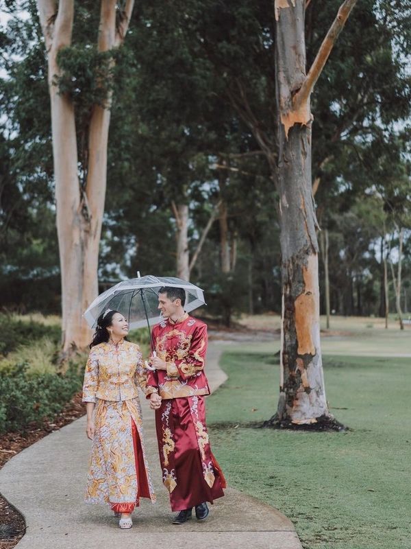 Couple in traditional attire walking under an umbrella on a park path.