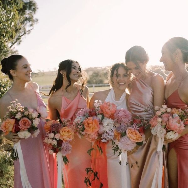 Five bridesmaids in pastel dresses holding colorful bouquets outdoors.