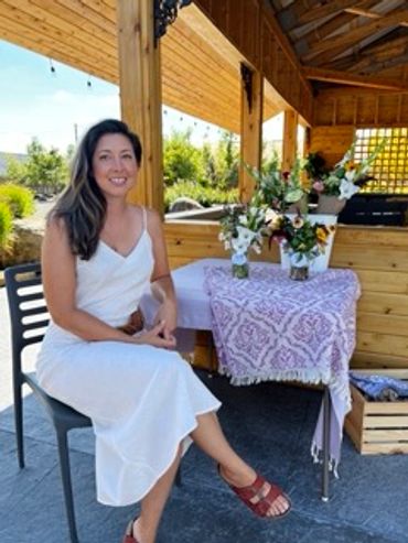 A woman in a white dress sits smiling under a wooden patio.