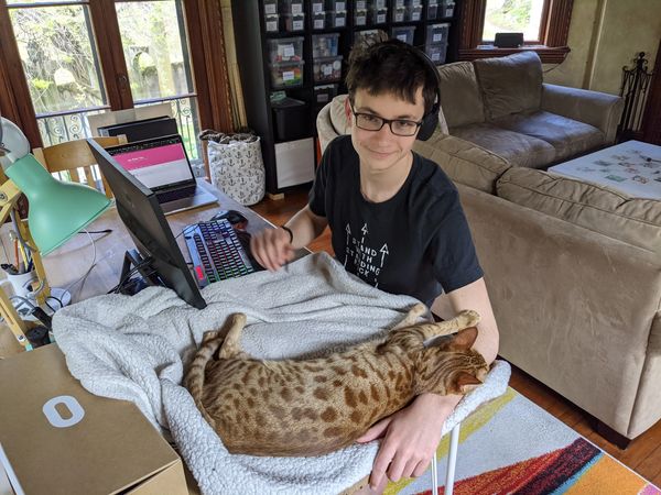 Isa working at his computer with a cat on his arm.