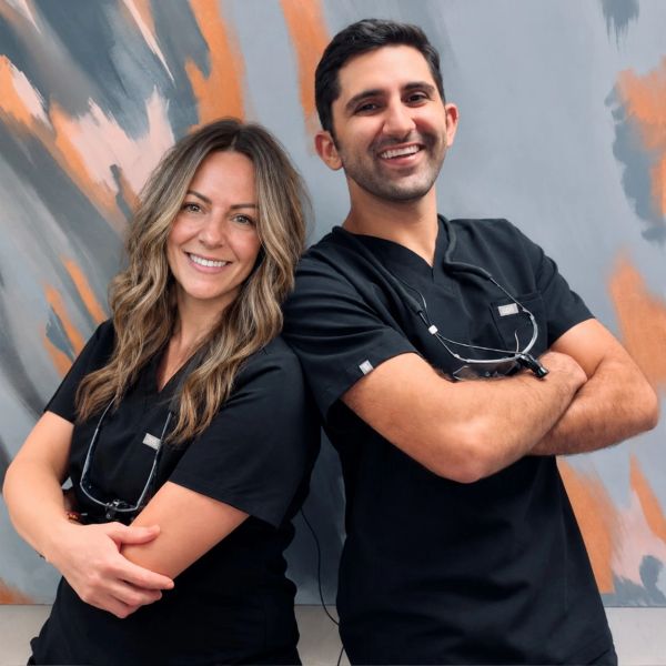 Two smiling dental professionals in black scrubs.