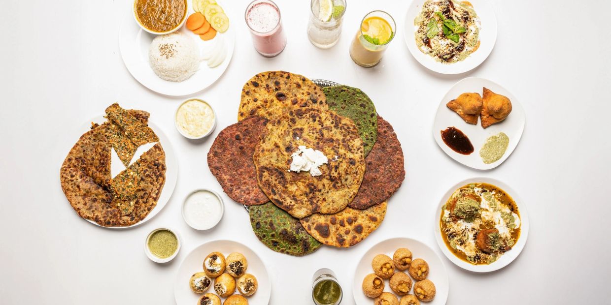 Assorted Indian breads and dishes arranged with drinks on a white background.