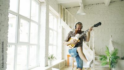 Man playing electric guitar enthusiastically in bright, modern room.