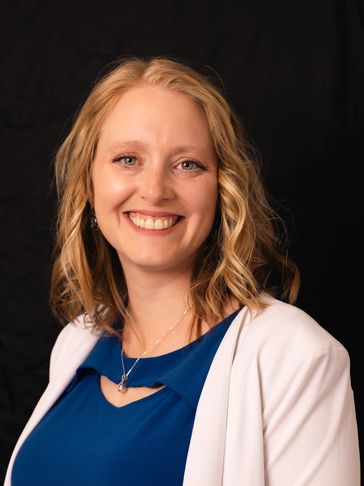 Smiling woman with blonde hair in blue dress and white blazer.
