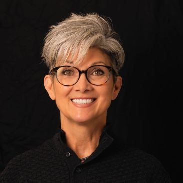 Smiling woman with short gray hair and glasses.
