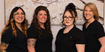A group of four smiling women in black tops.