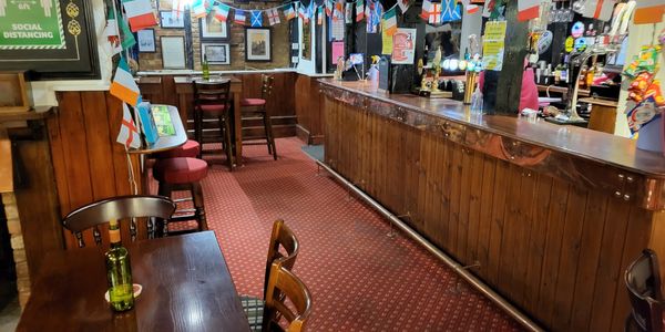 Cozy pub interior with wooden bar and festive flags.