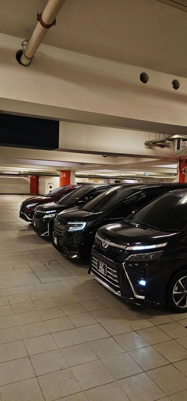 A row of sleek, black cars parked in an indoor garage with illuminated headlights.