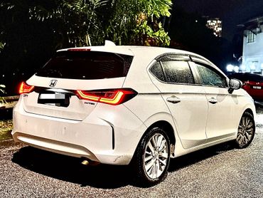 White Honda City hatchback parked on a wet road at night with illuminated tail lights.