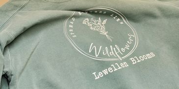 A pile of light green sweatshirts with "Lewellen Blooms" printed on them.