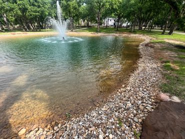 A serene pond with a fountain surrounded by trees and rocks.