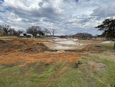 A partially excavated pond under a cloudy sky in a rural area.
