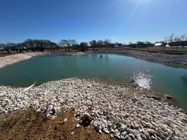 A man-made pond surrounded by rocks under a clear blue sky.