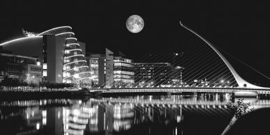Dublin city in black and white at night with the moon and the river in the foreground