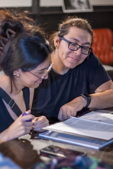 Two people studying together over documents at a table.