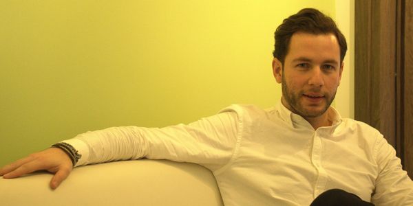 Manolis in a white shirt sitting casually on a white couch.