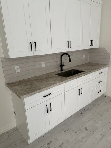 Modern kitchen cabinets with gray countertop and black faucet.