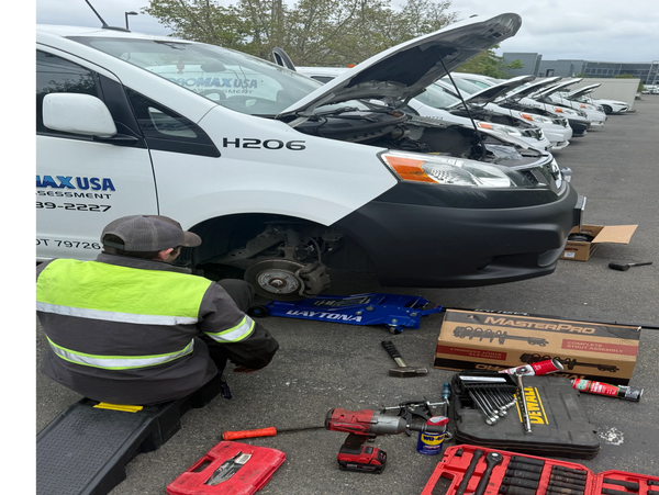 A mechanic repairs a white van with tools and parts spread on the ground.