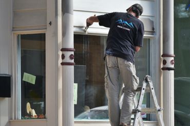 A worker on a ladder painting window trim.
