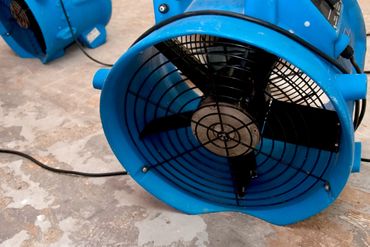 Two air mover blower fans in a basement drying out the room.
