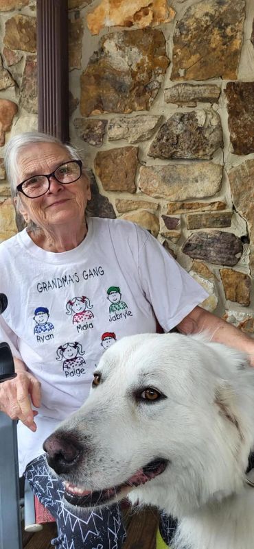 Smiling grandmother wearing a "Grandma's Gang" shirt with a large white dog.