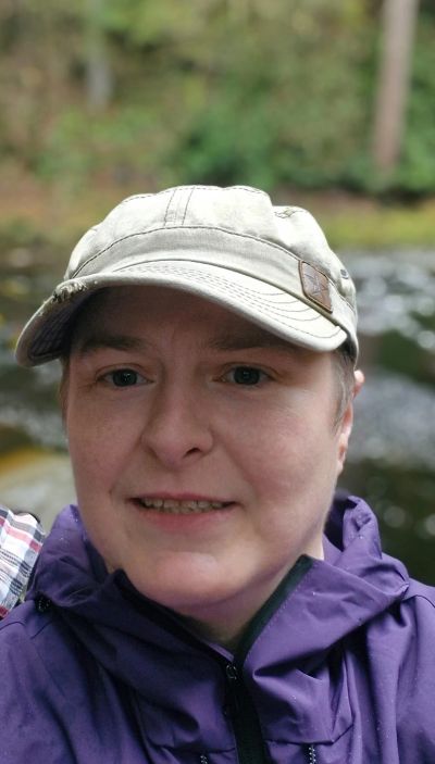 Person wearing a gray cap and purple jacket smiling outdoors.