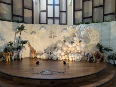 A safari-themed event stage decorated with white balloons and animal figures.