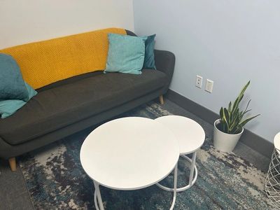 Cozy sitting area with a gray sofa, white nested tables, and a potted plant on a patterned rug.