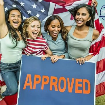 Four women smiling and holding a large "APPROVED" sign in front of a large American flag.
