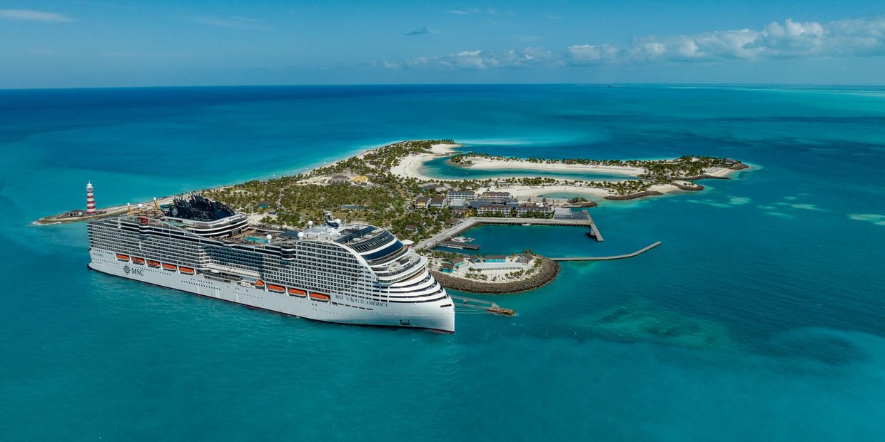 A large cruise ship docked near a tropical island with clear blue waters.
