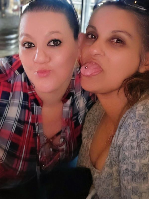 Two women posing for a close-up selfie, one playfully sticking out her tongue.