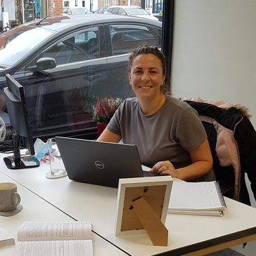 Woman smiling while working on a laptop at a desk.