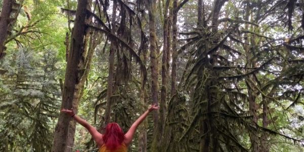 Person with red hair raising arms in a dense forest.