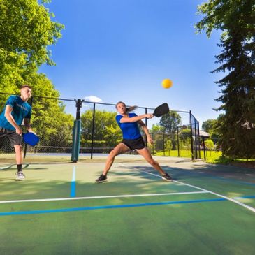 Two people playing pickleball outdoors on a sunny day.