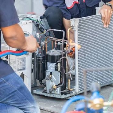 Technicians repairing an air conditioning unit using a torch and tools.